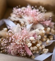 Boutonnières de mariage en fleurs séchées roses et beige présentées dans une boîte en carton.